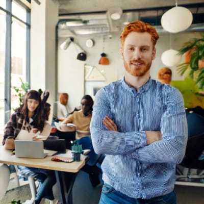 Jonge man met rood haar in een moderne werkruimte met collega's op de achtergrond