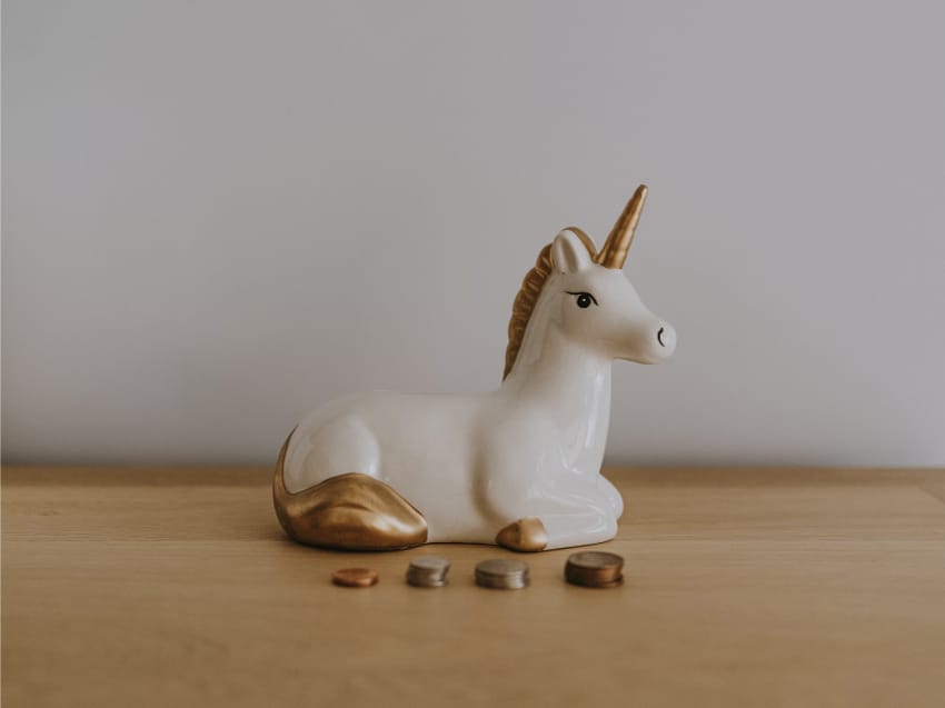 Witte eenhoorn spaarpot met muntjes ervoor – symbool voor zakgeld en sparen voor kinderen.