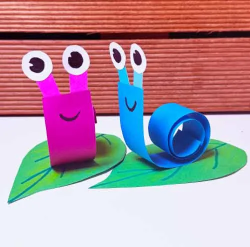 Twee papieren slakken op groene blaadjes, gemaakt met opgerolde papierstroken.