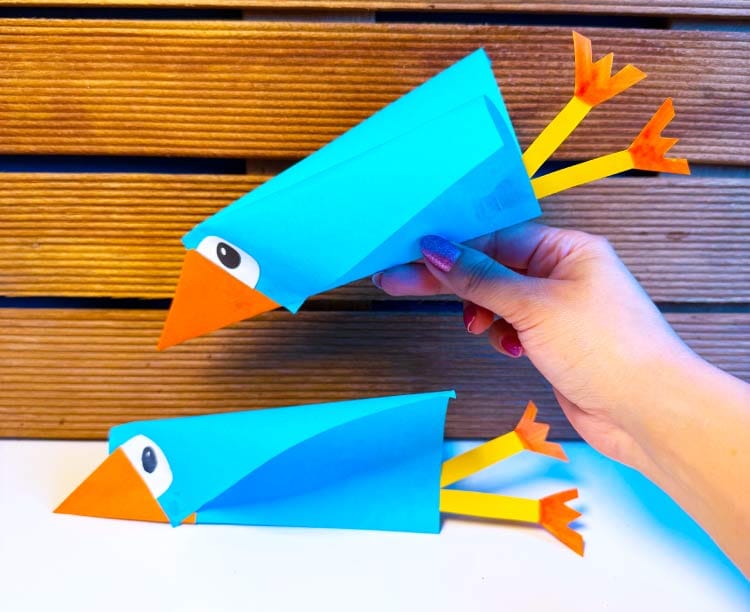 Vogel knutselen van papier met blauwe vleugels, oranje snavel en papieren poten